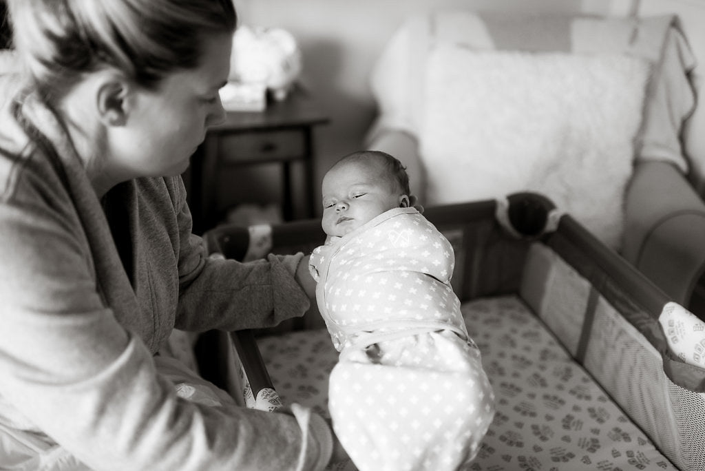 Mom putting baby in swaddle into bassinet