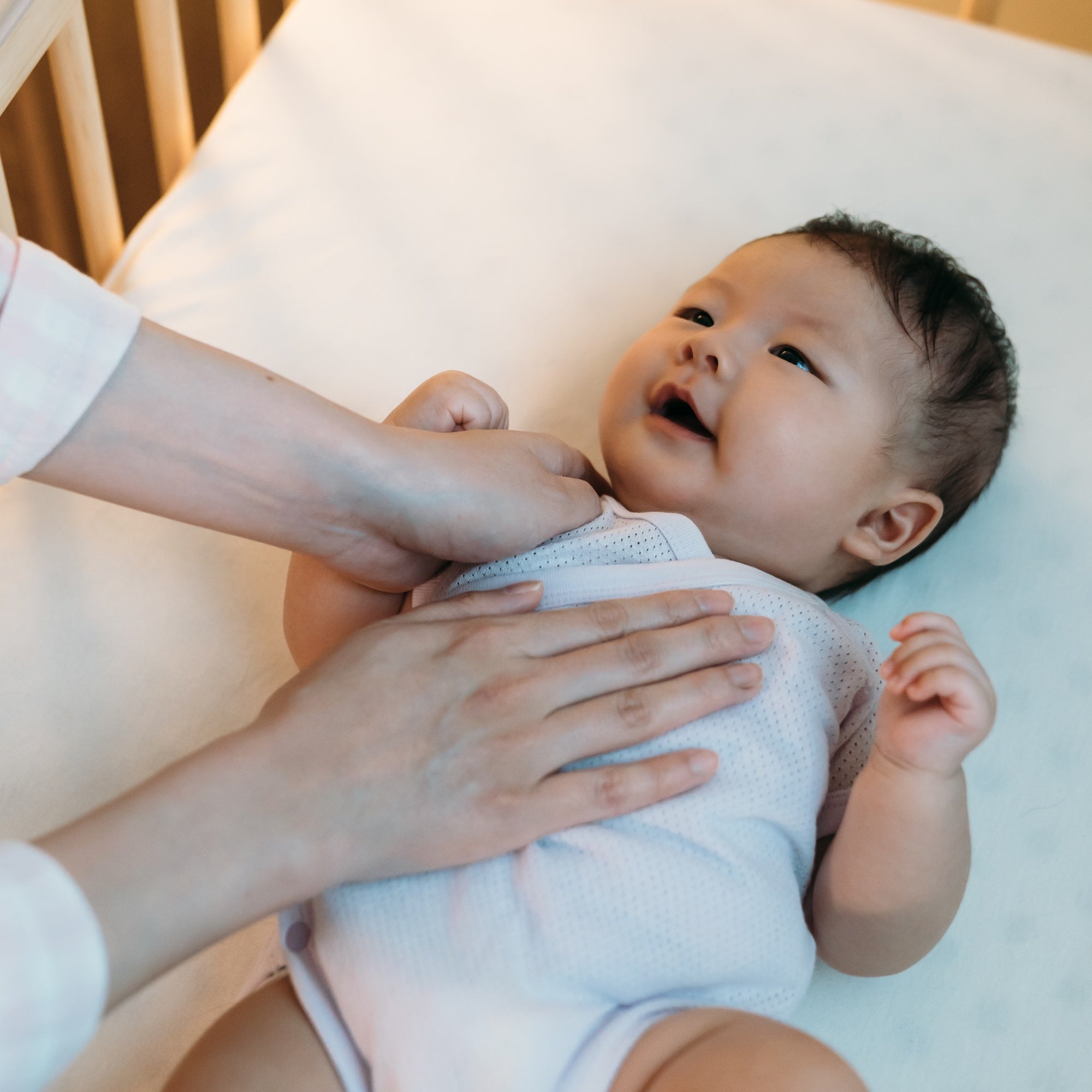 Smiling baby staring at mom as she gently places the baby down on the baby mattress