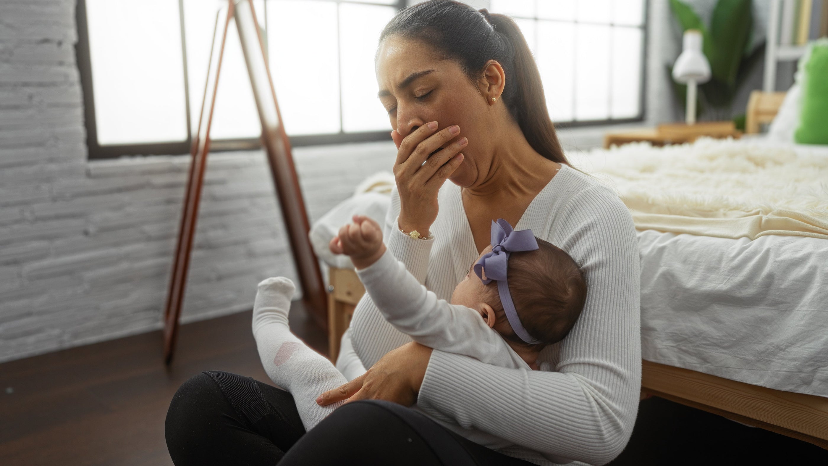 Tired mom yawning in bedroom, holding infant