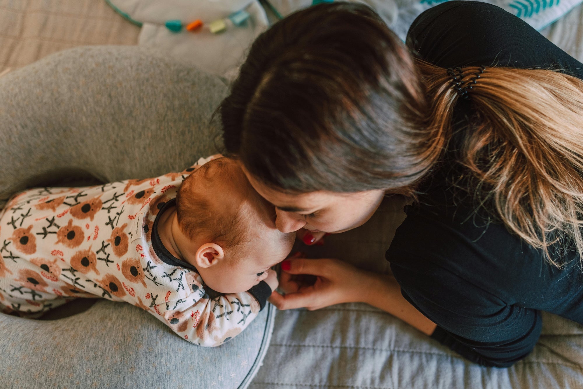 mom kissing baby on head with baby on boppy pillow for tummy time.